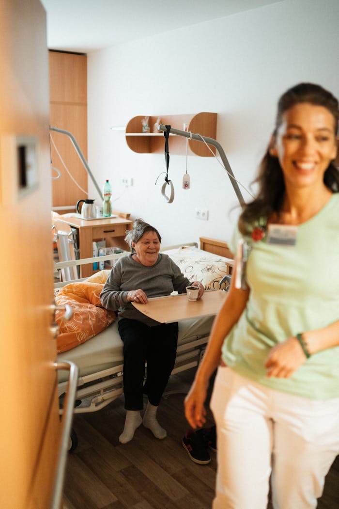 gallery-4 Smiling nurse assists senior patient in a cozy hospital room, promoting healthcare and wellbeing.