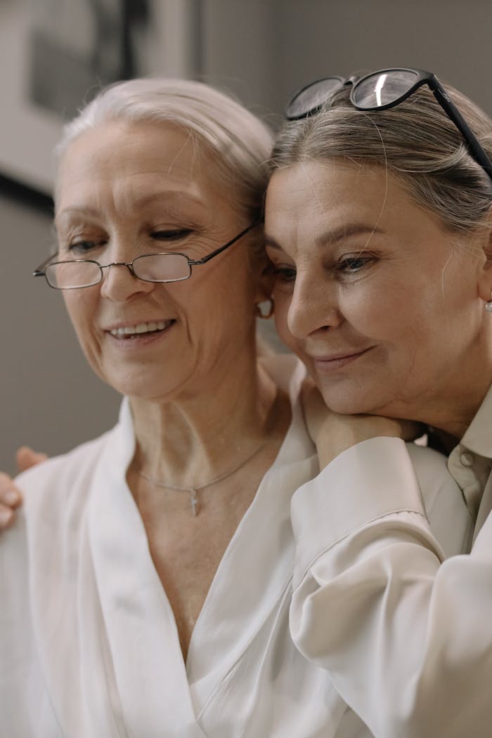 gallery-1 Two senior women embracing and smiling indoors, showcasing friendship and joy.